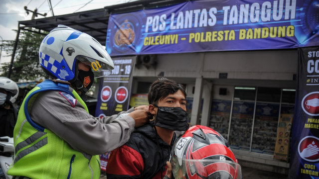 Petugas kepolisian memakaikan masker kepada seorang pengendara saat operasi kepatuhan memakai masker di Posko Lantas Tangguh, Cileunyi, Kabupaten Bandung, Jawa Barat, Rabu (10/2). Foto: Raisan Al Farisi/ANTARA FOTO