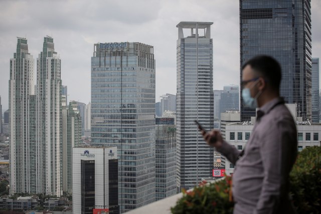 Karyawan melihat telepon selulernya dengan latar belakang gedung bertingkat di kawasan Jalan Jenderal Sudirman, Jakarta. Foto: Dhemas Reviyanto/ANTARA FOTO