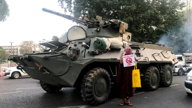 Seorang biksu Buddha memegang sebuah tanda berdiri di samping kendaraan lapis baja selama protes terhadap kudeta militer, di Yangon, Myanmar, Minggu (14/2). Foto: Stringer/REUTERS