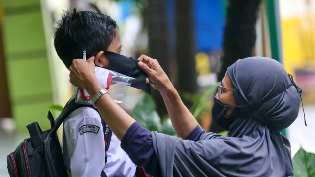 Seorang ibu memakaikan masker kepada anaknya saat masuk sekolah. Foto: Suparta/acehkini