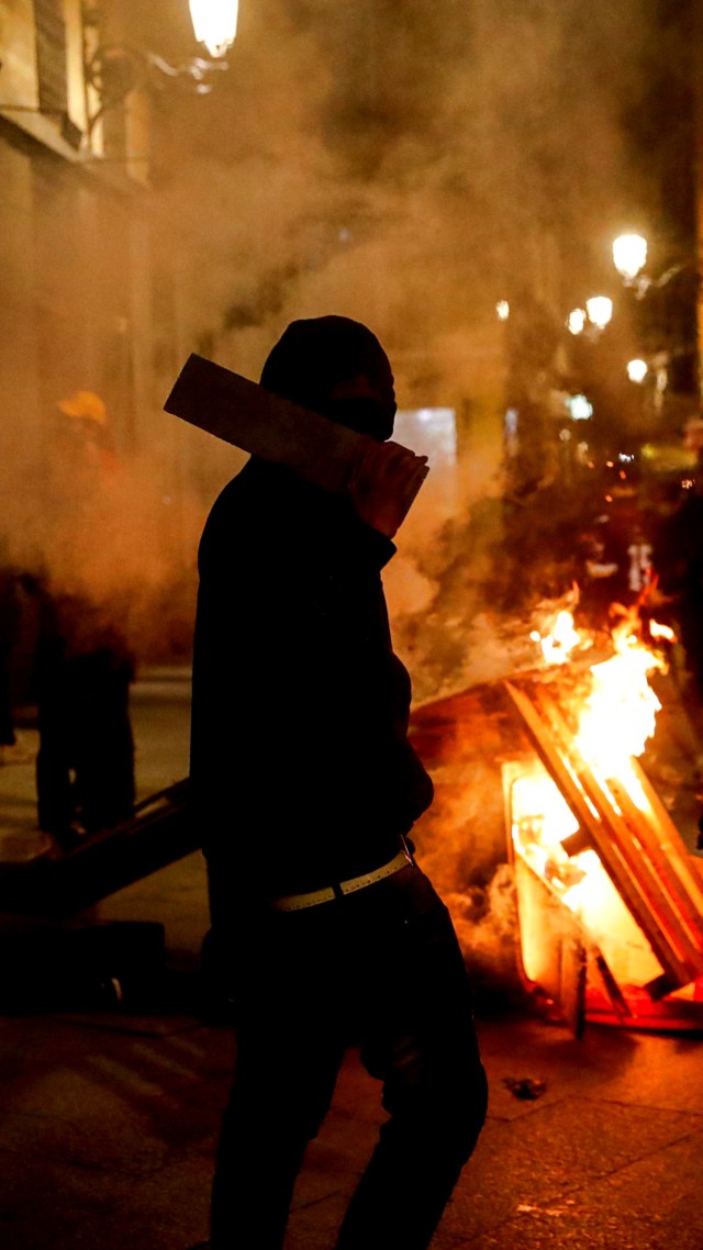 Seorang demonstran berdiri di dekat kobaran api saat aksi protes penangkapan rapper Catalan Pablo Hasel di Madrid, Spanyol, Rabu (17/2). Foto: Susana Vera/REUTERS