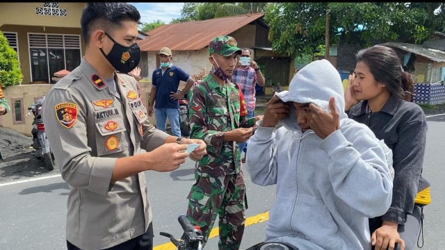 Kapolsek Tobelo saat membagikan masker ke masyarakat yang melewati jalan Desa Gorua Utara, Halmahera Utara. Foto: Polsek Tobelo.