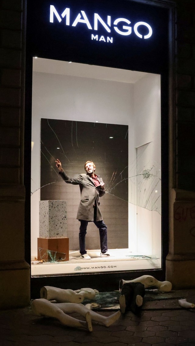 Seorang pria berpose di jendela toko yang rusak di samping makenin yang rusak, selama protes menentang penangkapan penyanyi rap Pablo Hasel di Barcelona, Spanyol, Sabtu (20/2). Foto: Nacho Doce/REUTERS