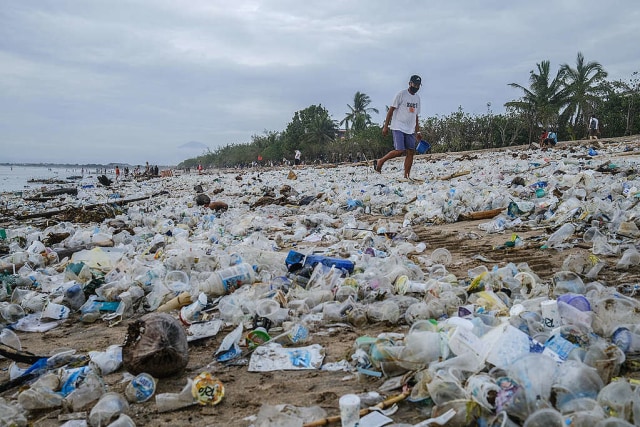 Seorang turis berjalan-jalan di pantai Kuta yang ikonik di Bali yang terkubur oleh sampah plastik selama musim hujan di Denpasar, Bali. Pantai Bali dipenuhi sampah plastik yang menjadi acara tahunan karena cuaca monsun, pengelolaan sampah yang buruk dan krisis pencemaran laut global. © Made Nagi / Greenpeace