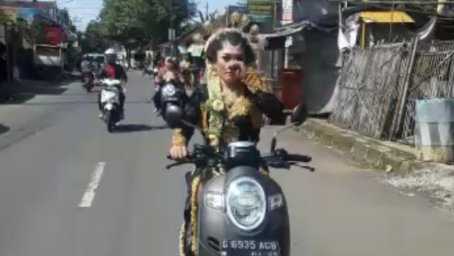  Seorang perempuan bergaun pengantin adat Jawa mengendarai sepeda motor matic.