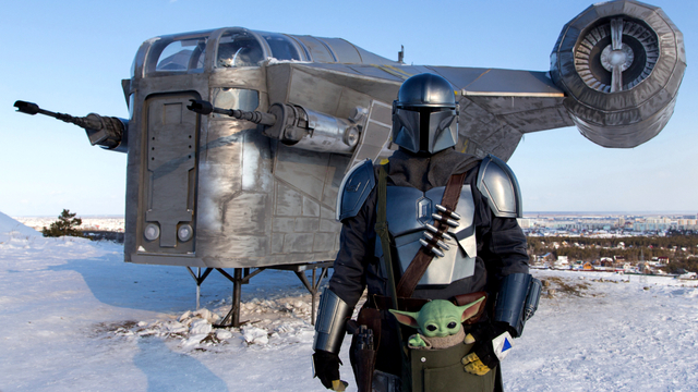 Seorang pria yang mengenakan kostum protagonis StarWars Din Djarin berpose di depan replika Razor Crest raksasa, sebuah pesawat tempur dari serial spin-off StarWars "The Mandalorian". Foto: EVGENIY SOFRONEYEV/AFP