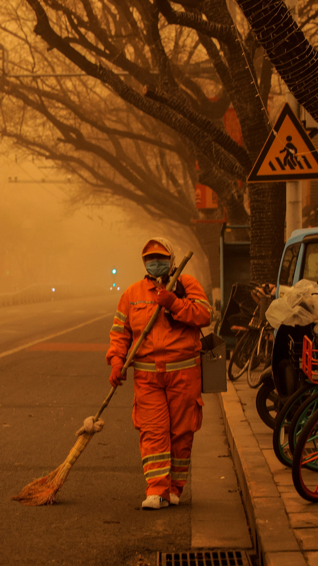 Seorang petugas kebersihan berjalan saat badai pasir melanda Beijing, China, Senin (15/3). Foto: Thomas Peter/REUTERS