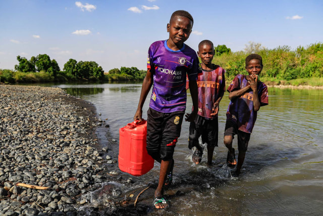 Seorang anak laki-laki yang mengenakan jersey Chelsea FC berjalan dengan jerigen keluar dari sungai Atbarah dekat desa Dukouli, Sudan (16/3/2021). Foto: ASHRAF SHAZLY/AFP