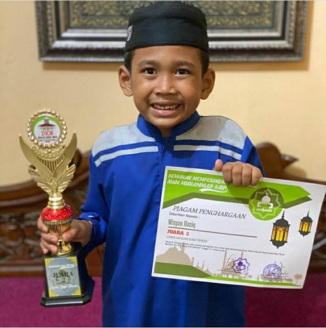 SENYUMAN anak Ustad Abdul Somad (UAS), Mizyan Hadziq saat berfoto dengan piala dan piagam penghargaan Juara II hafal ayat-ayat pendek Alquran. (Foto: Instagram: mizyanhadziq)