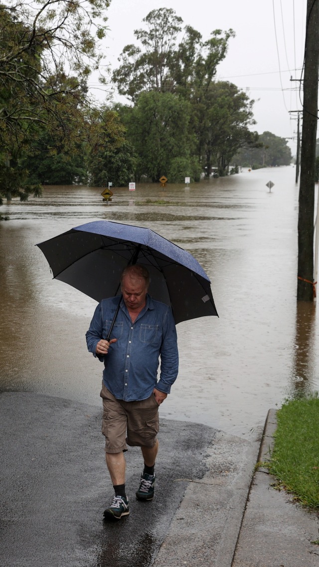 Seorang pria berjalan di jalan yang banjir di pinggiran kota Windsor, di negara bagian New South Wales, di Sydney, Australia, Senin (22/3). Foto: Loren Elliott/REUTERS