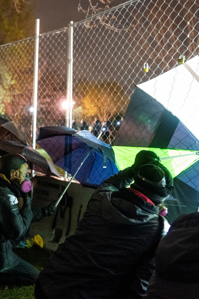 Demonstran yang menggunakan payung untuk menekan pagar keamanan perimeter dan menghasut kemarahan polisi di luar Departemen Kepolisian Brooklyn Center, Minneapolis, AS, Jumat (16/4). Foto: John Minchillo/AP Photo