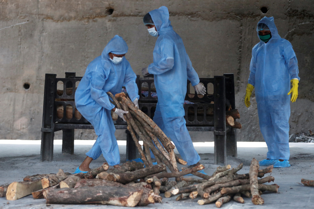 Pekerja mengenakan alat pelindung diri (APD) menyiapkan kayu untuk pemakaman jenazah yang meninggal karena virus corona di sebuah krematorium, Mumbai, India, Kamis (15/4).  Foto: Francis Mascarenhas REUTERS