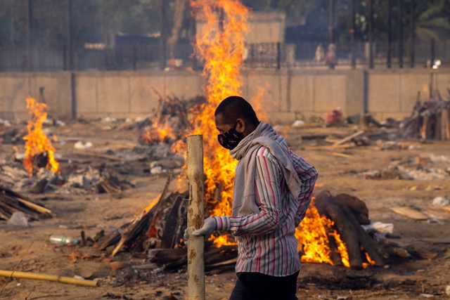 Seorang pria berjalan melewati pembakaran tumpukan kayu saat proses kremasi massal jenazah pasien COVID-19 di New Delhi, India. Foto: Danish Siddiqui/REUTERS