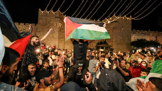 Warga Palestina mengibarkan bendera dan merayakan usai dicopotnya penghalang di luar Gerbang Damaskus di sekitar Kota Tua Yerusalem, Minggu (25/4). Foto: Ammar Awad/REUTERS