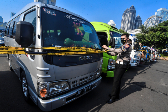 Petugas kepolisian memasang batas garis polisi saat mengamankan barang bukti kendaraan travel gelap di Lapangan Presisi Dit Lantas PMJ, Jakarta, Kamis (29/4). Foto: Muhammad Adimaja/ANTARA FOTO