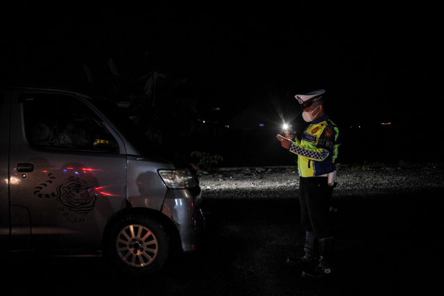 Petugas kepolisian memeriksa kelengkapan surat dari pengendara yang memiliki kendaraan dengan pelat nomor luar Garut di perbatasan Kabupaten Bandung dan Kabupaten Garut, Kadungora, Kabupaten Garut, Jawa Barat, Rabu (5/5/2021) malam. Foto: Raisan Al Farisi/ANTARA FOTO