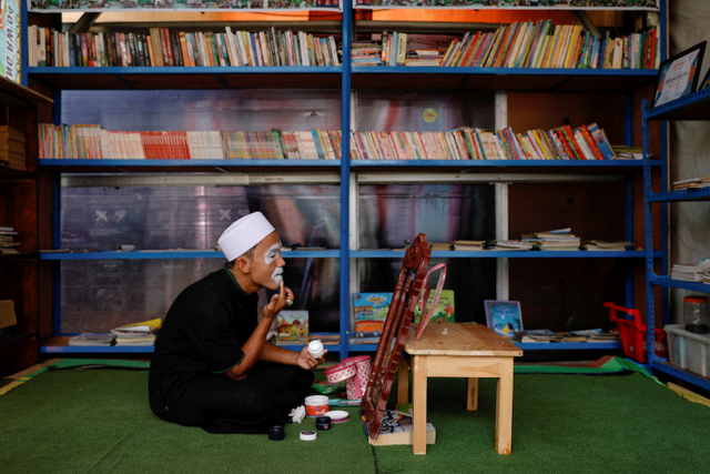 Yahya Edward Hendrawan, merias wajah saat bersiap untuk berpakaian badut sebelum mengajar di Kota Tangerang, Banten. Foto: Willy Kurniawan/REUTERS
