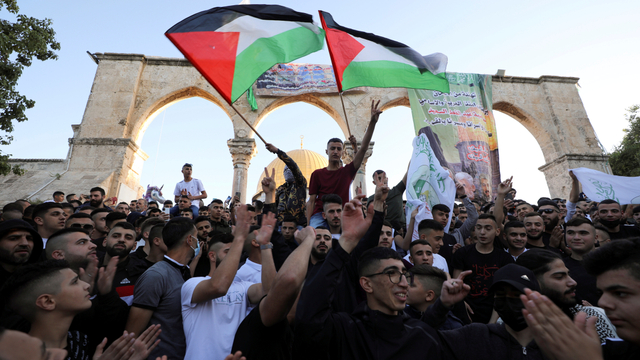 Orang-orang mengibarkan bendera Palestina selama pelaksanaan salat Idul Fitri, di kompleks masjid Al-Aqsa di Yerusalem, Kamis (13/5). Foto: Ammar Awad/REUTERS