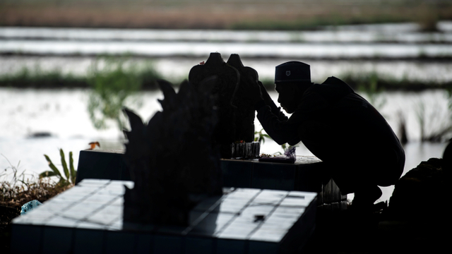 Warga berdoa di depan pusara keluarganya saat ziarah kubur. Foto: Muhammad Adimaja/ANTARA FOTO