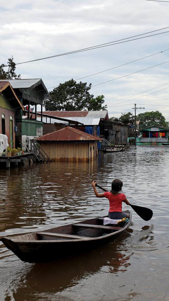 Seorang bocah melintas dengan perahu di jalan yang banjir akibat sungai Solimoes yang naik, di Anama, negara bagian Amazonas, Brasil (13/5). Foto: Bruno Kelly/REUTERS