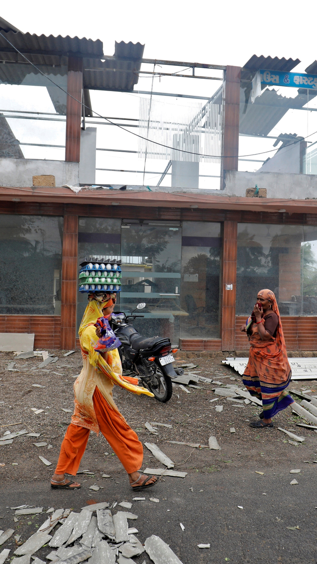 Seorang wanita yang membawa telur berjalan melewati bangunan komersial yang rusak setelah Topan Tauktae melanda, di Kodinar, di negara bagian barat Gujarat, India, Selasa (18/5). Foto: Amit Dave/REUTERS