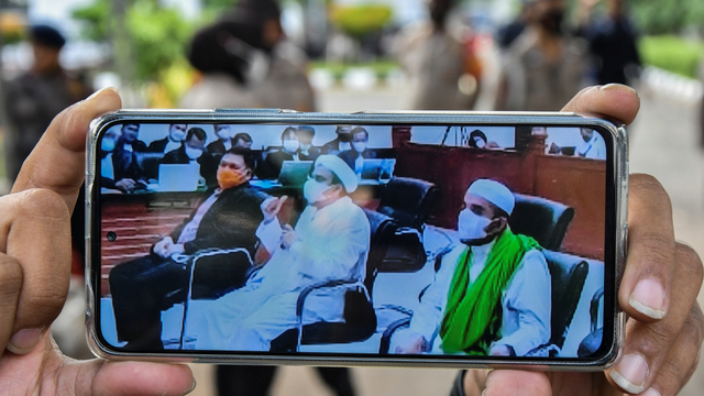 Layar telepon pintar menampilkan suasana sidang yang dihadiri Habib Rizieq Shihab (tengah), Direktur rumah sakit UMMI Andi Tatat (kiri) dan Habib Hanif Alatas (kanan) di Pengadilan Negeri Jakarta Timur, Kamis (27/5/2021). Foto: Fakhri Hermansyah/ANTARA FOTO