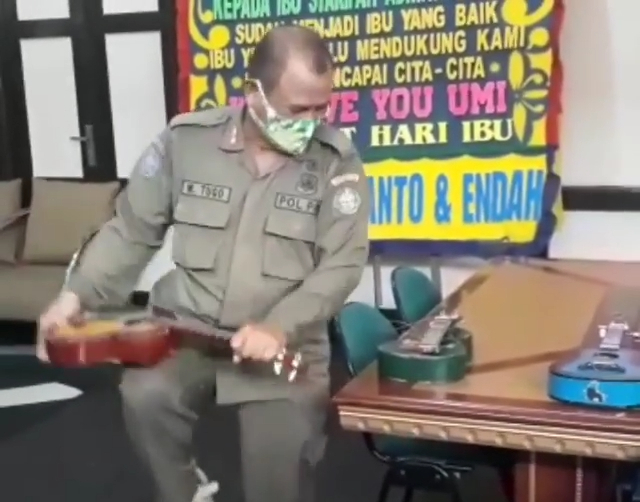 Seorang personel Satpol PP Kota Pontianak mematahkan gitar ukulele milik pengamen yang terjaring razia. Aksi ini mendapat kecaman dari netizen. Foto: Dok Hi!Pontianak
