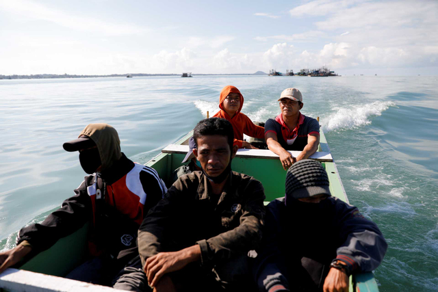 Hendra, seorang penambang timah berusia 51 tahun, duduk di atas perahu kayu bersama para penambang lainnya saat mereka menuju ke ponton, 1 Mei 2021. Foto: Willy Kurniawan/REUTERS