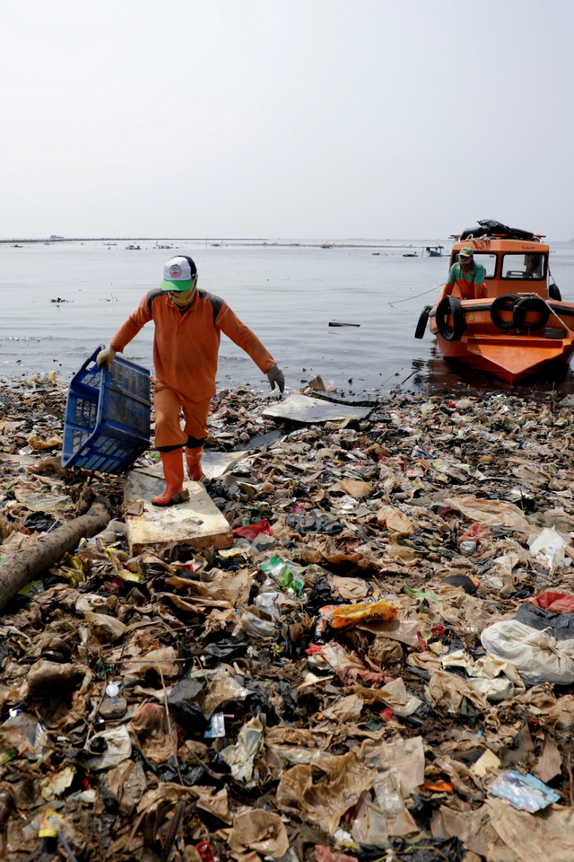 Petugas kebersihan berjalan di antara sampah-sampah yang menumpuk di sepanjang pantai Jakarta, Selasa (8/6). Foto: Willy Kurniawan/REUTERS