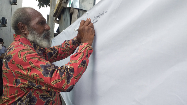 Tokoh adat Merauke, Johanes Gluba Gebze saat menandatangani kain putih untuk dukungan deklarasi Provinsi Papua Selatan. (BumiPapua.com/Abdel Syah) 