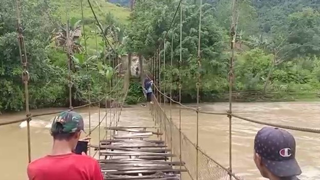 Warga di Desa Pamoseang, Kabupaten Mamasa, Sulawesi Barat, menyeberangi sungai dengan menggantung di tali karena kondisi jembatan gantung rusak. Foto: Tangkapan Layar Video