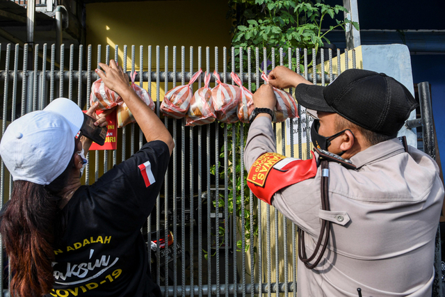 Anggota satuan tugas penanganan COVID-19 bersama Polisi menggantungkan makanan di pagar rumah warga yang menjalani isolasi mandiri di kawasan Warakas. Foto: M Risyal Hidayat/Antara Foto