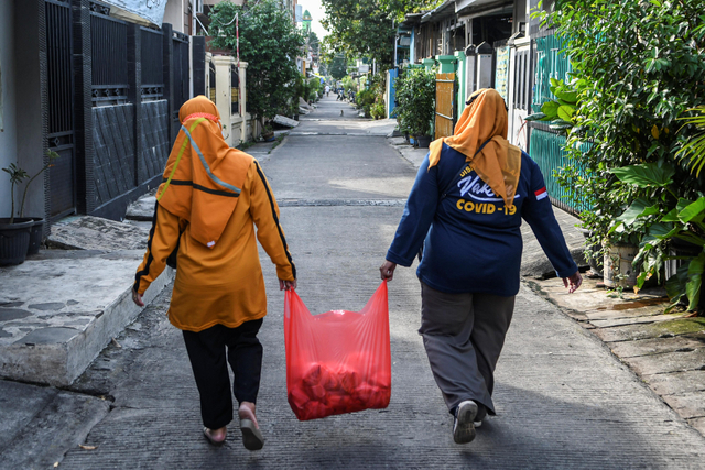 Anggota satuan tugas penanganan COVID-19 bersama Polisi berjalan dengan membawa makanan yang akan diberikan pada warga yang menjalani isolasi mandiri di kawasan Warakas. Foto: M Risyal Hidayat/Antara Foto