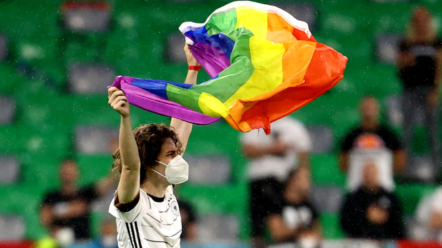 Seorang pengunjuk rasa memegang bendera pelangi di lapangan sebelum pertandingan Jerman vs Hongaria di Arena Sepak Bola Munich, Munich, Jerman, Rabu (23/6). Foto: Pool via REUTERS/Kai Pfaffenbach