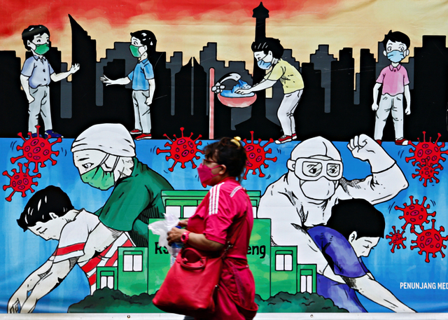 Seorang wanita mengenakan masker pelindung berjalan melewati mural yang mempromosikan kesadaran akan wabah penyakit coronavirus. Foto: REUTERS/Ajeng Dinar Ulfiana