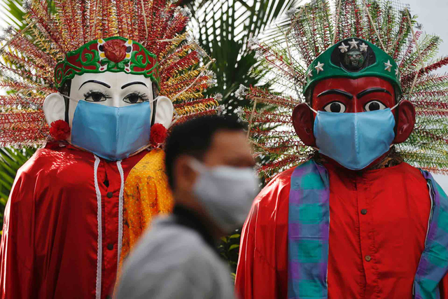 Seorang pria yang mengenakan masker pelindung berjalan melewati figur boneka besar tradisional yang disebut "Ondel-ondel" yang juga mengenakan masker (30/6/2021). Foto: Willy Kurniawan/REUTERS