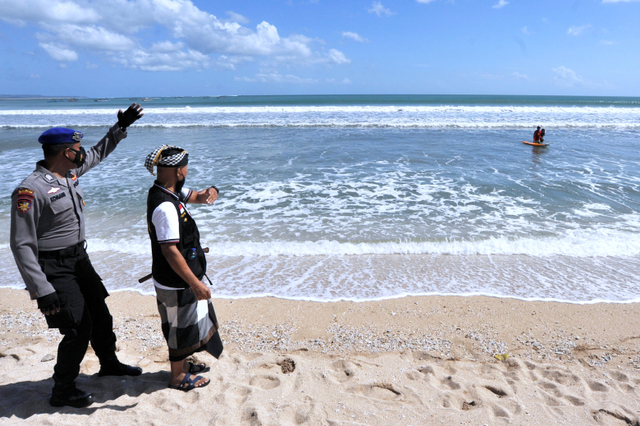 Polisi bersama Pecalang atau petugas keamanan adat Bali meminta wisatawan untuk meninggalkan kawasan wisata Pantai Kuta di Badung, Bali, Sabtu (3/7/2021). Foto: Fikri Yusuf/Antara Foto