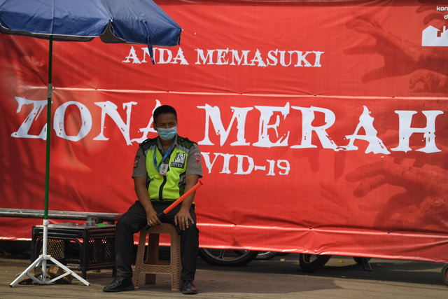 Seorang petugas keamanan berjaga dengan latar belakang spanduk pemberitahuan lokasi zona merah COVID-19 di Depok, Jawa Barat, Rabu (7/7/2021). Foto: Wahyu Putro A/Antara Foto