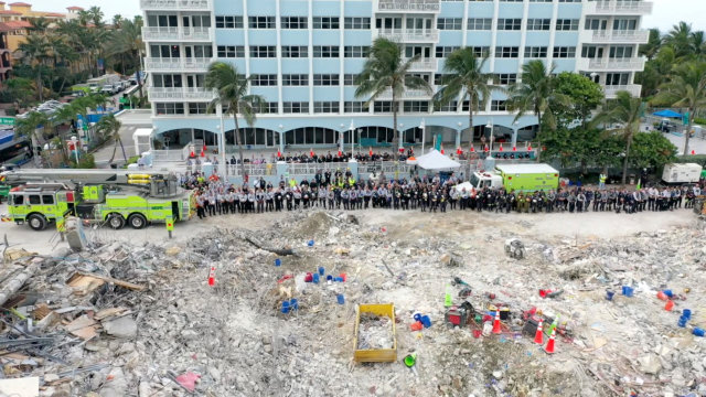 Anggota tim SAR berdiri saat mengheningkan cipta dan berdoa di depan puing-puing gedung Champlain Towers South yang runtuh di Surfside, Florida, Amerika Serikat. Foto: Miami-Dade Fire Rescue/Reuters