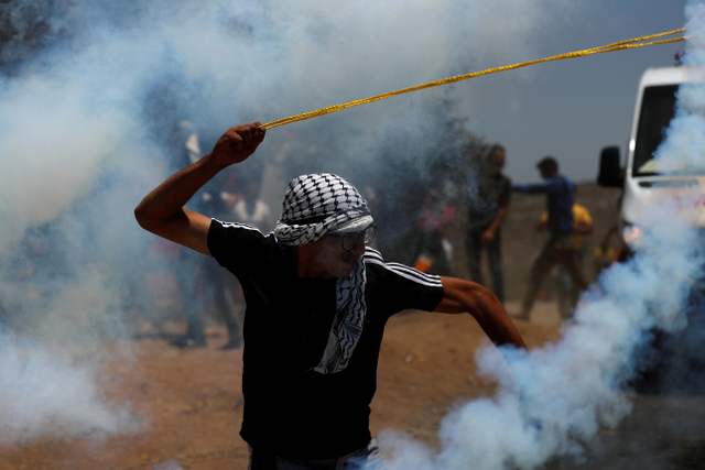 Demonstran Palestina menggunakan ketapel melawan pasukan Israel saat protes terhadap pemukiman yang diduduki Israel di Beita, di Tepi Barat. Foto: Mohamad Torokman/Reuters