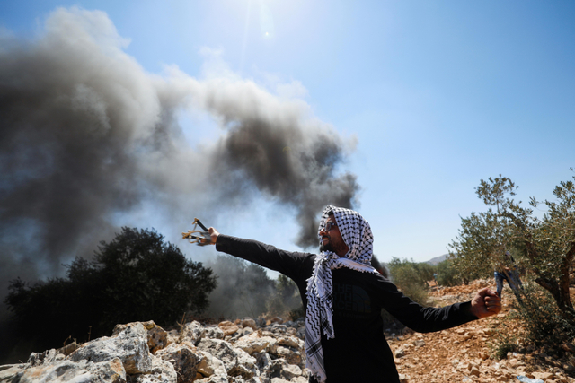 Demonstran Palestina menggunakan ketapel melawan pasukan Israel saat  protes terhadap pemukiman yang diduduki Israel di Beita, di Tepi Barat. Foto: Mohamad Torokman/Reuters