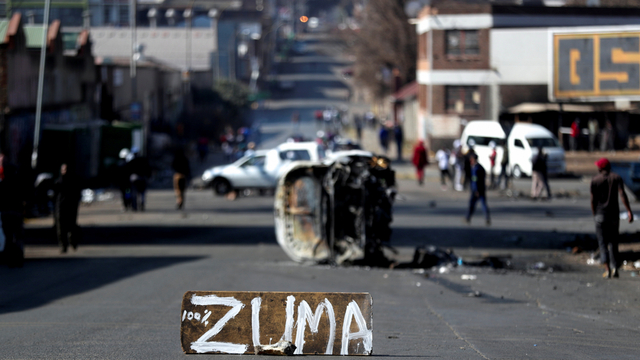 Sisa-sisa mobil yang terbakar dan sebuah tanda memblokir jalan saat aksi unjuk rasa di jalan-jalan di Johannesburg, Afrika Selatan, Minggu (11/7). Foto: Sumaya Hisham/REUTERS