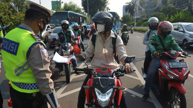 Polisi mengamati surat milik pengendara sepeda motor saat akan melintas di titik penyekatan baru di kawasan Gerbang Pemuda, Jakarta Selatan, Jumat (16/7/2021). Foto: M Risyal Hidayat/ANTARA FOTO
