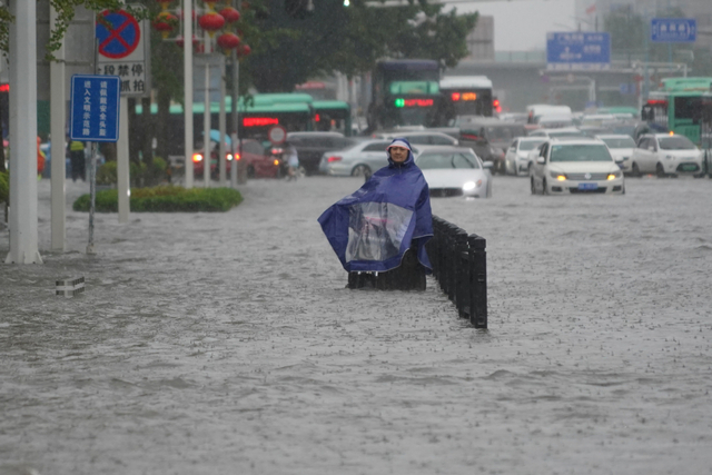 Seorang warga mengenakan penutup hujan berdiri di jalan banjir di Zhengzhou, provinsi Henan, China.  Foto: cnsphoto/via REUTERS