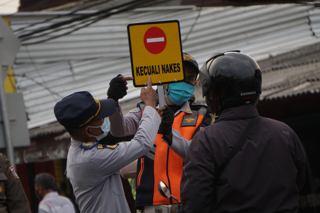 Petugas menujukan tanda yang boleh melintas saat penyekatan di perbatasan Jakarta-depok pada pelaksanaan PPKM darurat. Foto: Jamal Ramadhan/kumparan