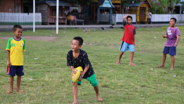 Seorang anak dengan tawa semringahnya di Kelurahan Tanah Beru, Bulukumba, Sulawesi Selatan yang sedang bermain Australian Football bersama teman-temannya. Sumber: dokumentasi pribadi