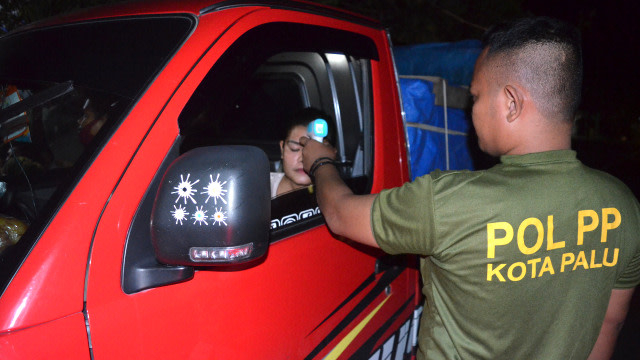 Salah satu petugas Satpol PP Kota Palu memeriksa suhu tubuh pengendara yang mengangkut bahan kebutuhan pokok saat masuk wilayah Kota Palu. Foto: Humas Pemkot Palu