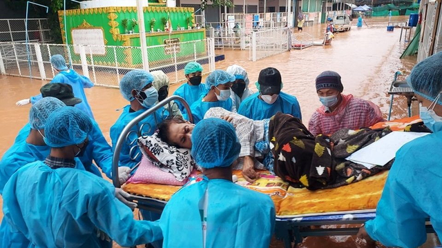 Relawan dengan mengenakan alat pelindung diri (APD) membawa pasien COVID-19 yang terbaring di ranjang saat banjir melanda wilayah Myawaddy, Myanmar. Foto: Karen Information Center/via REUTERS