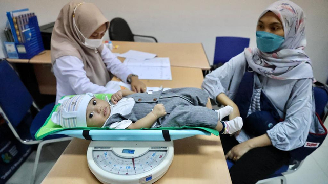 Seorang ibu membawa anaknya untuk menerima imunisasi di Puskesmas Ulee Kareng, Kota Banda Aceh, Senin (16/8/2021). Foto: Suparta/acehkini