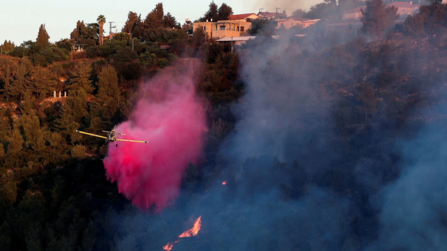 Sebuah pesawat pemadam kebakaran menyebarkan bahan penghambat api saat membantu memadamkan api di dekat desa Israel Beit Meir, pinggiran Yerusalem, Senin (16/8). Foto: Ammar Awad/REUTERS